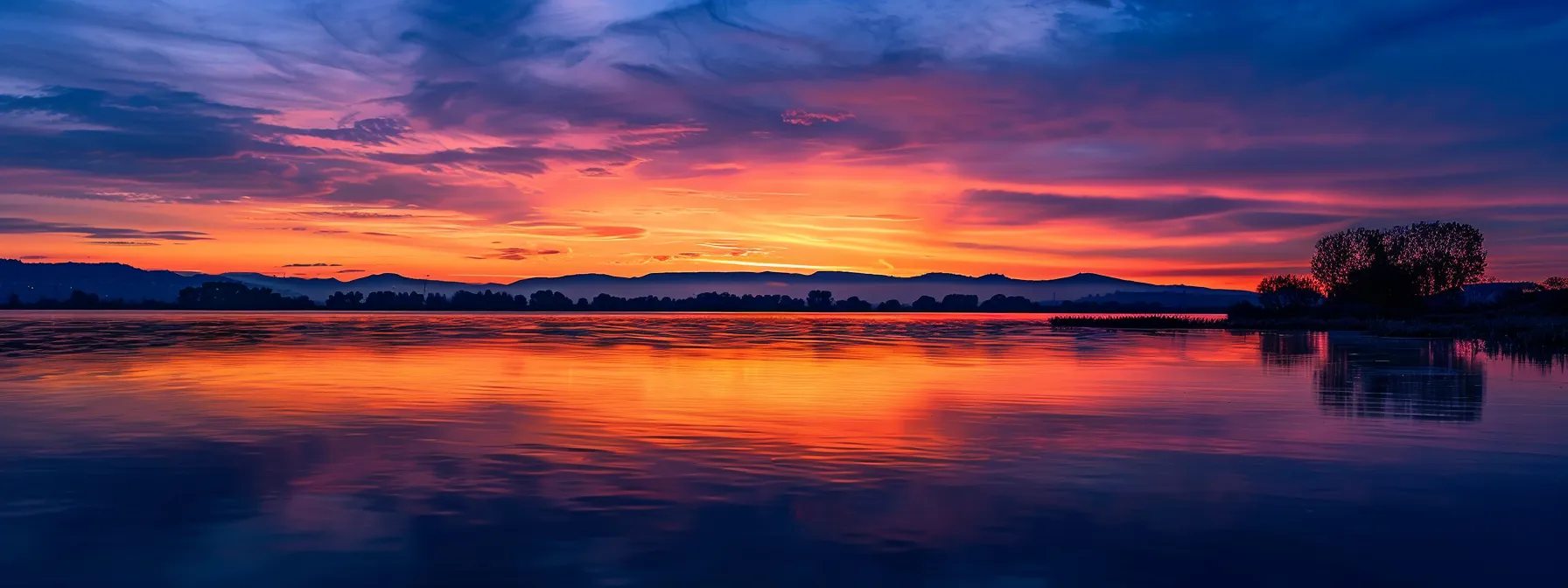 a breathtaking sunset casts vibrant hues of orange and purple over a serene lake, where the tranquil reflections create a stunning symphony of colors against the still water.