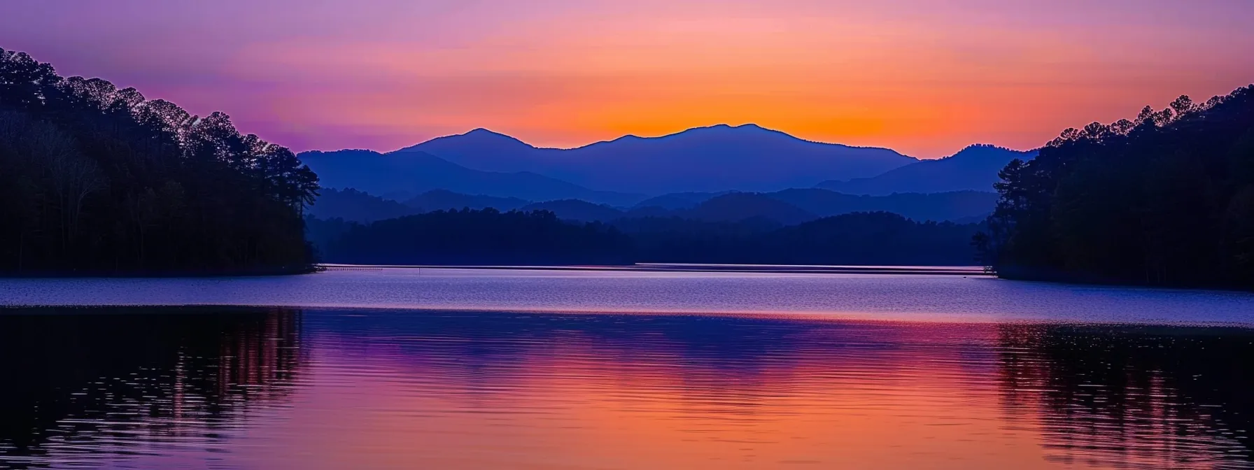 a breathtaking sunset casts vibrant hues of orange and purple across a serene lake, with silhouettes of majestic mountains reflecting on the water's glassy surface.