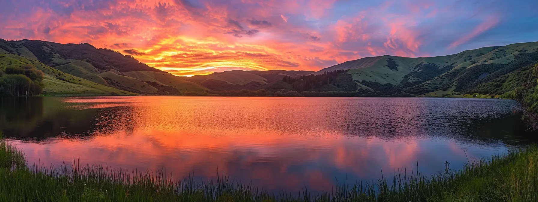 a breathtaking sunset illuminates a tranquil mountain lake, casting vibrant oranges and purples across the sky, with the still water perfectly reflecting the fiery hues above.