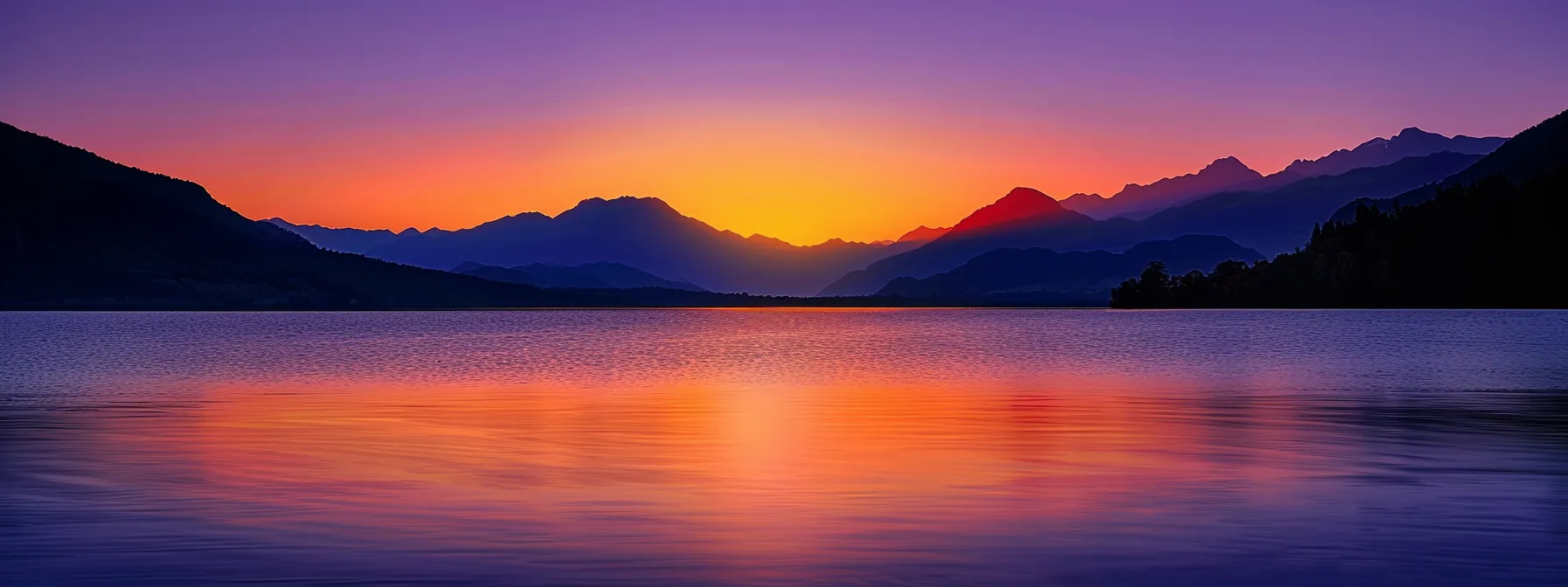a breathtaking view of a vibrant sunset casting brilliant hues of orange and purple across a serene lake, surrounded by silhouetted mountains under a clear sky.