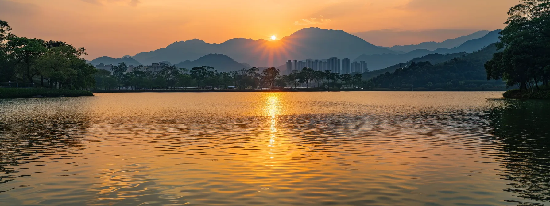 a radiant sunset casts a golden glow over a tranquil lake, its smooth surface reflecting the vibrant hues of orange and pink as silhouettes of distant mountains loom majestically in the background.