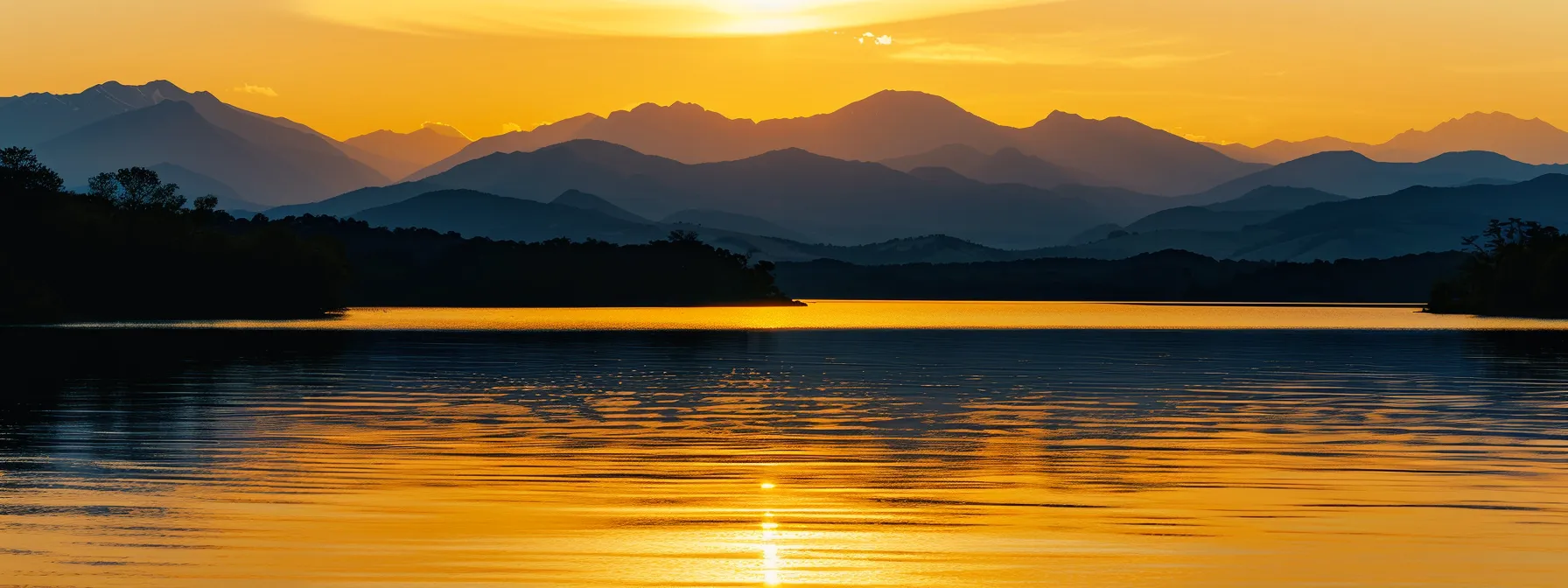 a vibrant sunset casts a warm golden hue over a tranquil lake, reflecting the silhouettes of majestic mountains in the background.