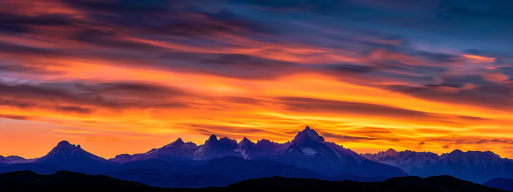 a vibrant sunset casts a warm golden glow over a serene mountain landscape, with towering peaks silhouetted against the colorful sky.