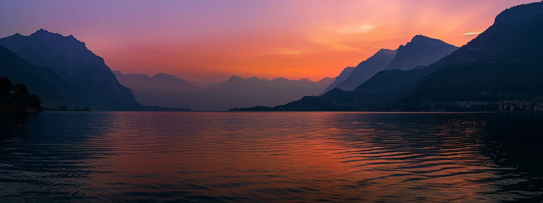 a vibrant sunset paints the sky in shades of orange and purple, casting a golden glow over a tranquil lake, where silhouettes of distant mountains reflect on the shimmering water's surface.